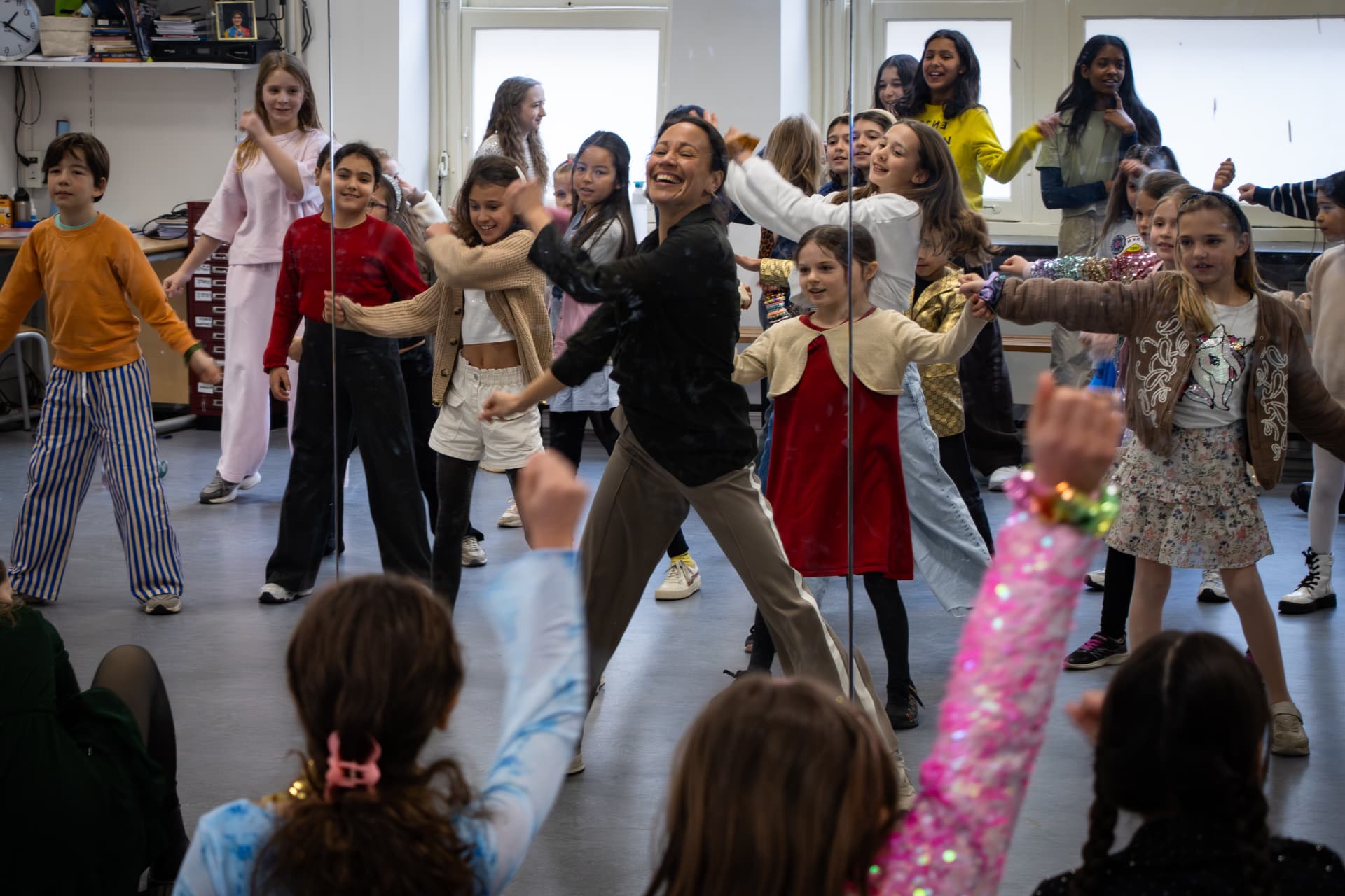 Dansdocent danst samen met een grote groep kinderen in de dansles